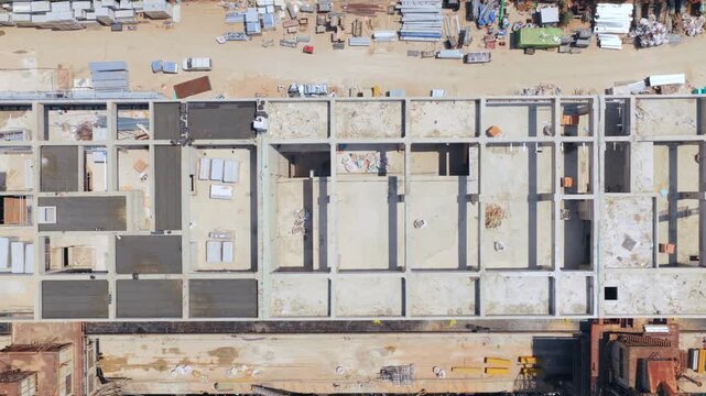 High angle drone footage showing the development of a large building's concrete foundation and structure on a waterfront property, with materials and machinery visible along the pier
