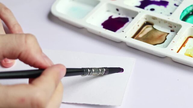 Artist painting with watercolor on paper using water to create soft texture and color effects. Close up of paintbrush blending wet paint in home studio during creative painting process	