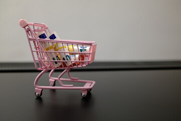 Rolled 10 euro banknotes in pink toy shopping cart on dark surface with copy space © Stanislava