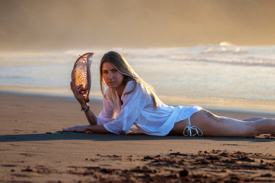 Woman lying on beach holding hat during sunset