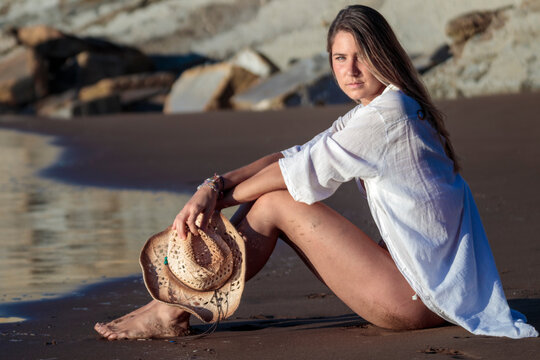 Woman sitting on beach holding straw hat relaxing