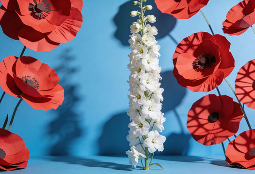 Paper poppy flowers, tall white delphinium bloom, floral craft setup, blue studio backdrop, papercraft floral arrangement, decorative craft flowers, floral design display, spring paper art.