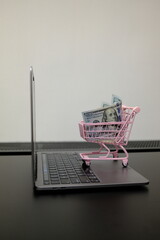 Pack of 100 US dollar bills in pink toy shopping cart on open laptop, online shopping and e-commerce concept © Stanislava