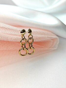 Pair of gold dangle earrings with interlocking rings. Elegant jewelry displayed with pink tulle and white satin fabric