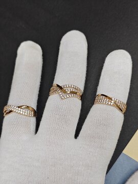 Gold rings with clear stones presented on a hand wearing a white inspection glove. Jewelry quality control and display. Black and blue background