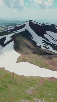 Vertical Drone Shot of Volcanic Crater Lake surrounded by Red Soil, Green Slopes, and Melting Snow