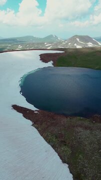 Vertical Drone Shot of Volcanic Crater Lake surrounded by Red Soil, Green Slopes, and Melting Snow