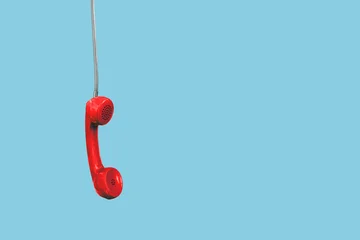 A red landline phone hangs by its cord  space available for text, isolated against a neutral background. © Igor Link