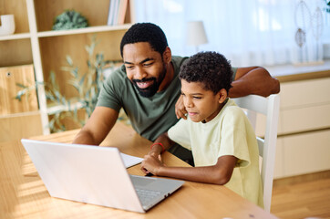 Fototapeta premium Father and son doing homework with laptop at home. Father and teenage son using laptop. Boy and dad sitting at home working with notebook