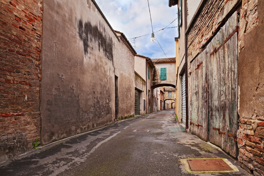 Narrow alley with old arches, rustic buildings and weathered wooden doors in a historic village, province of Ravenna, Emilia-Romagna, Italy