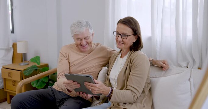 Senior couple browse tablet together on sofa, tapping and comparing image references before painting at home, combining supportive conversation, creative preparation, relaxation, and active aging.