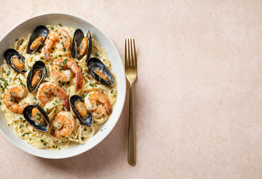 Seafood Pasta Dish with Shrimp and Mussels in Creamy Sauce Garnished with Herbs on Pink Surface for Culinary Backgrounds and Restaurant Menu Design