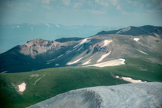 Panoramic Landscape of Volcanic Plateau with Red Earth Cone, Patchy Snow, and Fluffy Cumulus Clouds