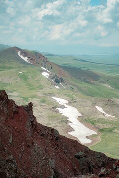 Panoramic Landscape of Volcanic Plateau with Red Earth Cone, Patchy Snow, and Fluffy Cumulus Clouds
