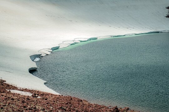 Aerial View of Alpine Crater Lake Edge with Emerald Water Transitioning to Deep Blue Deep