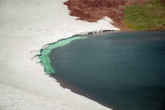 Aerial View of Alpine Crater Lake Edge with Emerald Water Transitioning to Deep Blue Deep