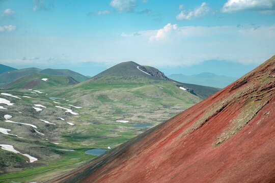 Panoramic Landscape of Volcanic Plateau with Red Earth Cone, Patchy Snow, and Fluffy Cumulus Clouds