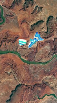 Flying above potash ponds, red rocks, deserted dry area with canyon of a river. Camera is zooming in. Vertical video. Animation based on image by NASA