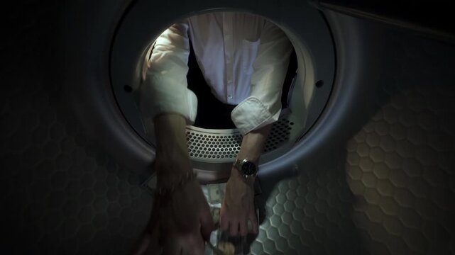 Conceptual video of an unrecognisable Caucasian man wearing a white shirt placing US dollar banknotes in a washing machine with his hands and taking them out in slow motion. Money Laundering Concept