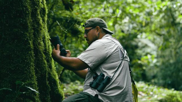 Latino wildlife photographer with binoculars carefully taking a macro picture of a tree covered in moss in Arenal Volcano National Park