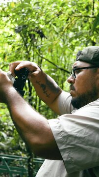 Male adventurer with a camera exploring the Arenal Volcano National Park. Young content creator filming wildlife in the tropical rainforest. Vertical