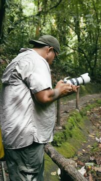 Young male photographer with a telephoto lens capturing images of nature while trekking on a trail in the lush rainforest of Costa Rica. Vertical