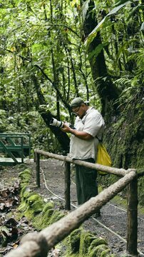 Wildlife photographer reviewing pictures on his camera display while standing on a path in the lush green jungle of Arenal Volcano National Park. Vertical