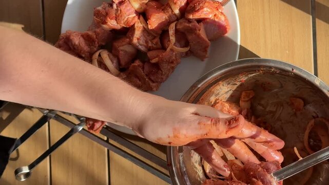 Hands marinating raw meat with red spice paste in metal bowl, overhead kitchen prep on wooden table, messy fingers and rustic cooking mood