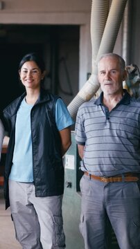 Two skilled craftspeople, a woman and a senior man, posing inside their family owned carpentry workshop. Colleagues standing together
