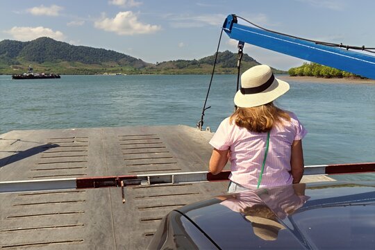 A woman standing on the outdoor deck of a slow-moving passenger ferry, looking out at the tropical sea. Female tourist enjoying the ocean breeze during an island-hopping vacation in Thailand. 