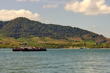 Fototapeta premium Modern passenger transport vessel navigating open ocean waters in Southeast Asia. Coastal scenery of Krabi province visible in the background with visible water wake. 