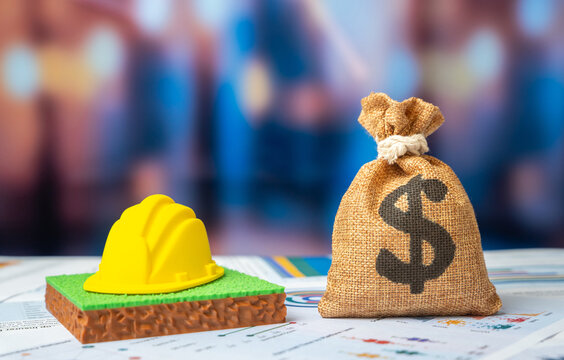 A dollar money bag and a plot of land with a hard hat. Construction budget.