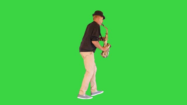 An elderly man walks in a funny manner playing the saxophone on a Green Screen, Chroma Key.