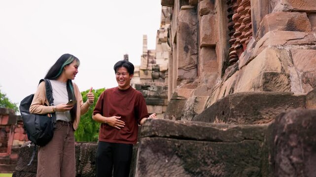 Young Asian backpackers walking and exploring historical stone temple site on sunny day. Travel destination adventure, historic archaeology discovery and summer vacation trip.