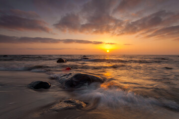 Obraz premium Sunset over rocky beach and gentle waves