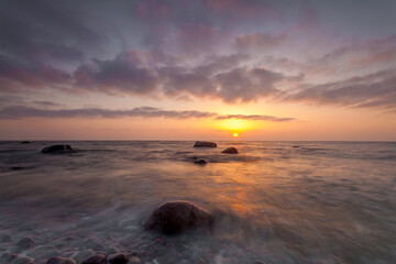 Obraz premium Sunset over rocky beach and gentle waves