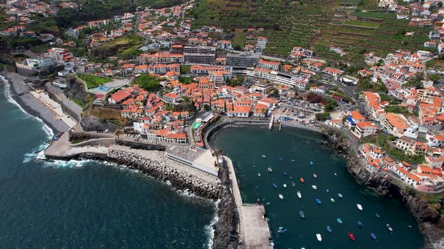 Madeira iconi coastal village Camara de Lobos drone semi-circle flight over the picturesque bay with traditional fishing boats and cozy orange houses, Portugal