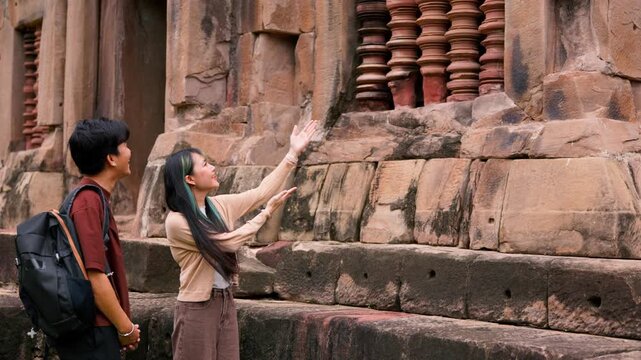 Young Asian backpackers walking and exploring historical stone temple site on sunny day. Travel destination adventure, historic archaeology discovery and summer vacation trip.