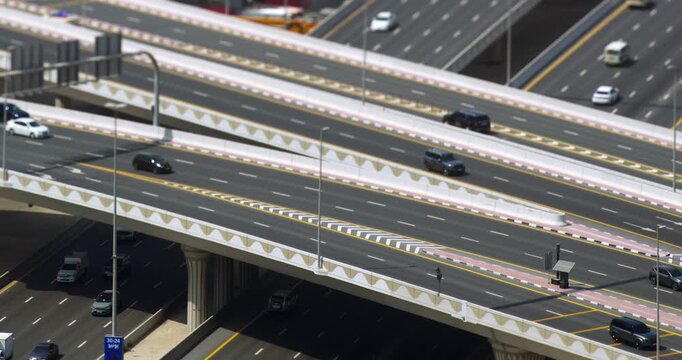 Dubai highway overpasses with car traffic, tilt shift miniature effect, elevated view of multi lane roads and bridges, sunny day, timelapse with slow zoom out of urban transport