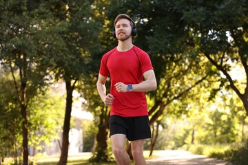 Fototapeta premium Man in sportswear with headphones running in park, low angle view