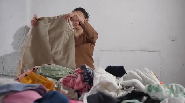 Woman sorting large piles of used clothes. Textile waste, fast fashion problem