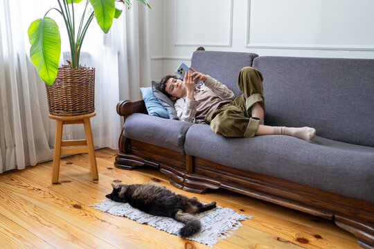 Lazy carefree woman resting on sofa spending peaceful weekend at home doom scrolling online on smartphone, boredom and tasks procrastination, relaxed female lying on couch browsing media on phone.