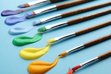 Different brushes with paints on light blue background, closeup © New Africa