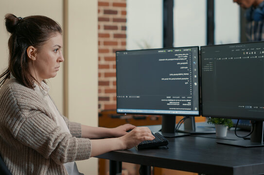 Focused programmer writes code while looking at multiple computer screens, with programming language algorithms and teamwork in the background.