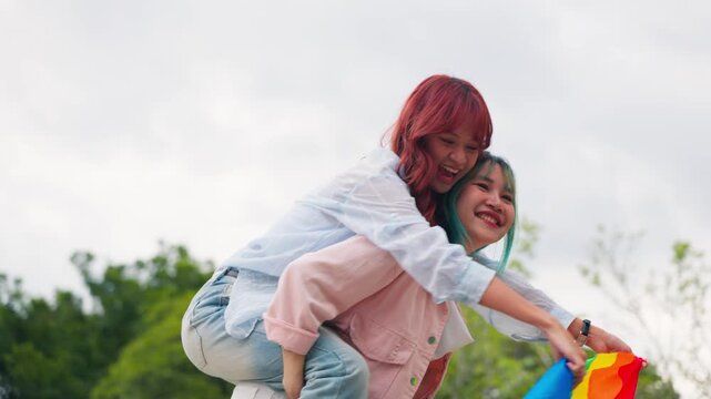 Asian LGBTQ women couple sharing happy moments and holding pride flag outdoors in park. Inclusive community, equality movement, diversity, and joyful relationship lifestyle.