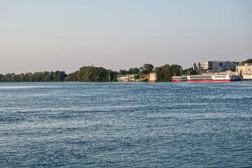 Obraz premium Rhone river flowing past arles coastline with a docked cruise ship at sunset