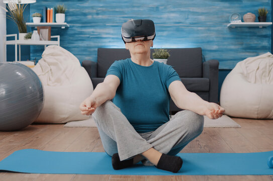 Senior woman meditates with VR headset on yoga mat during meditation on a yoga mat, combining virtual reality goggles with relaxation, wellness and senior fitness.