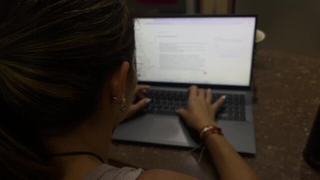 Young woman typing on laptop chatting with AI at desk