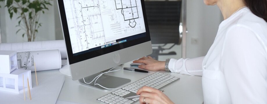 Architect woman working on blueprints and building plans using computer aided design in modern office. Business and architecture concept