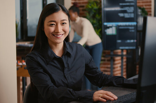 Asian software developer smiling and resuming work typing code on computer keyboard sitting at desk in big data office, with artificial intelligence and big data.